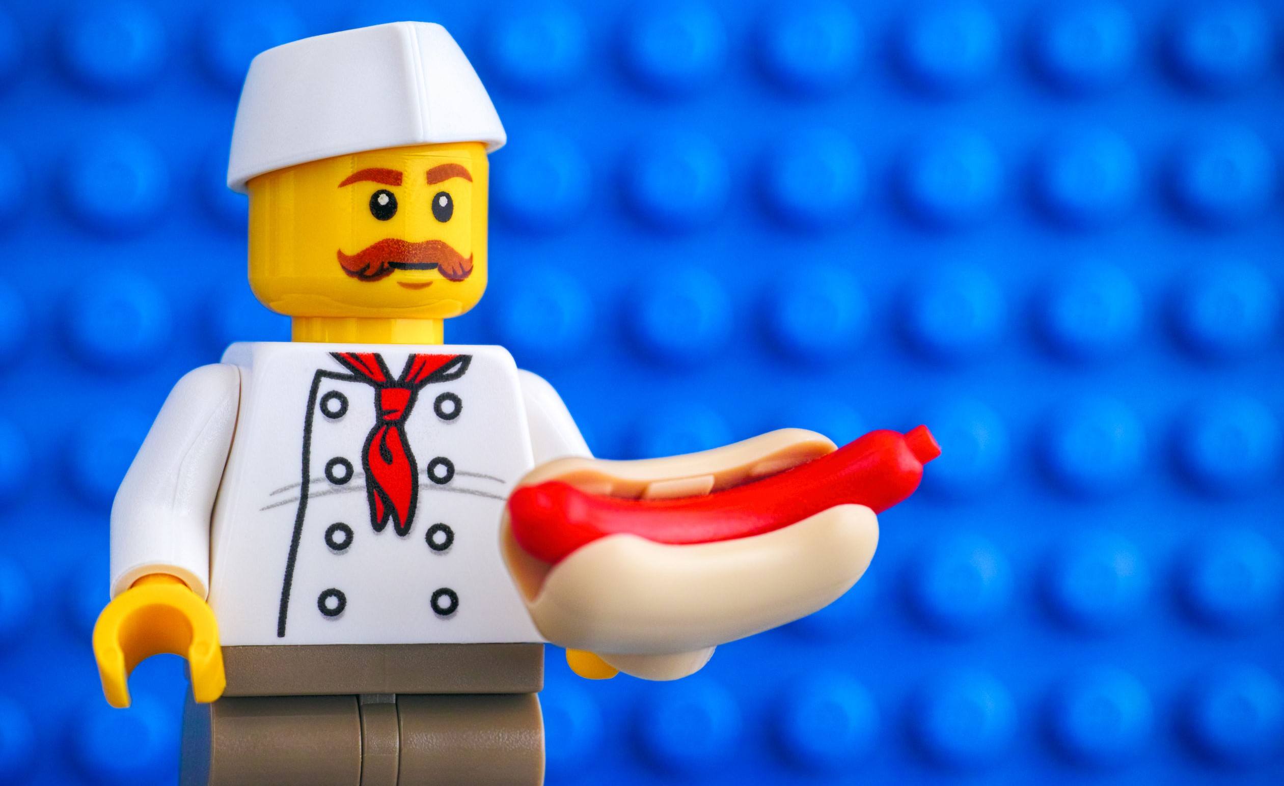Lego chef with hot dog against blue baseplate backgrounds.
