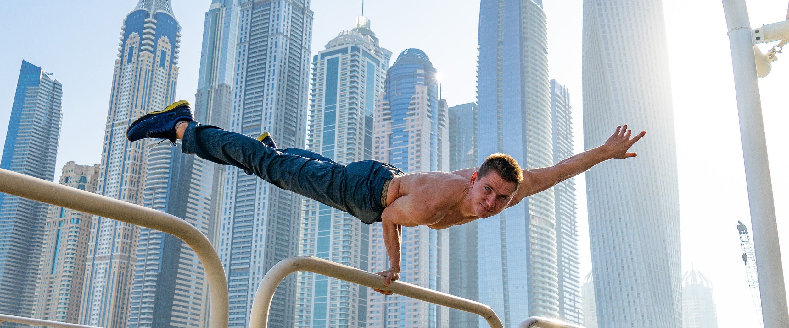 Muscular man doing workout on the street with cityscape of skyscrapers on preliminaries in Dubai. Concept of healthy lifestyle and modern