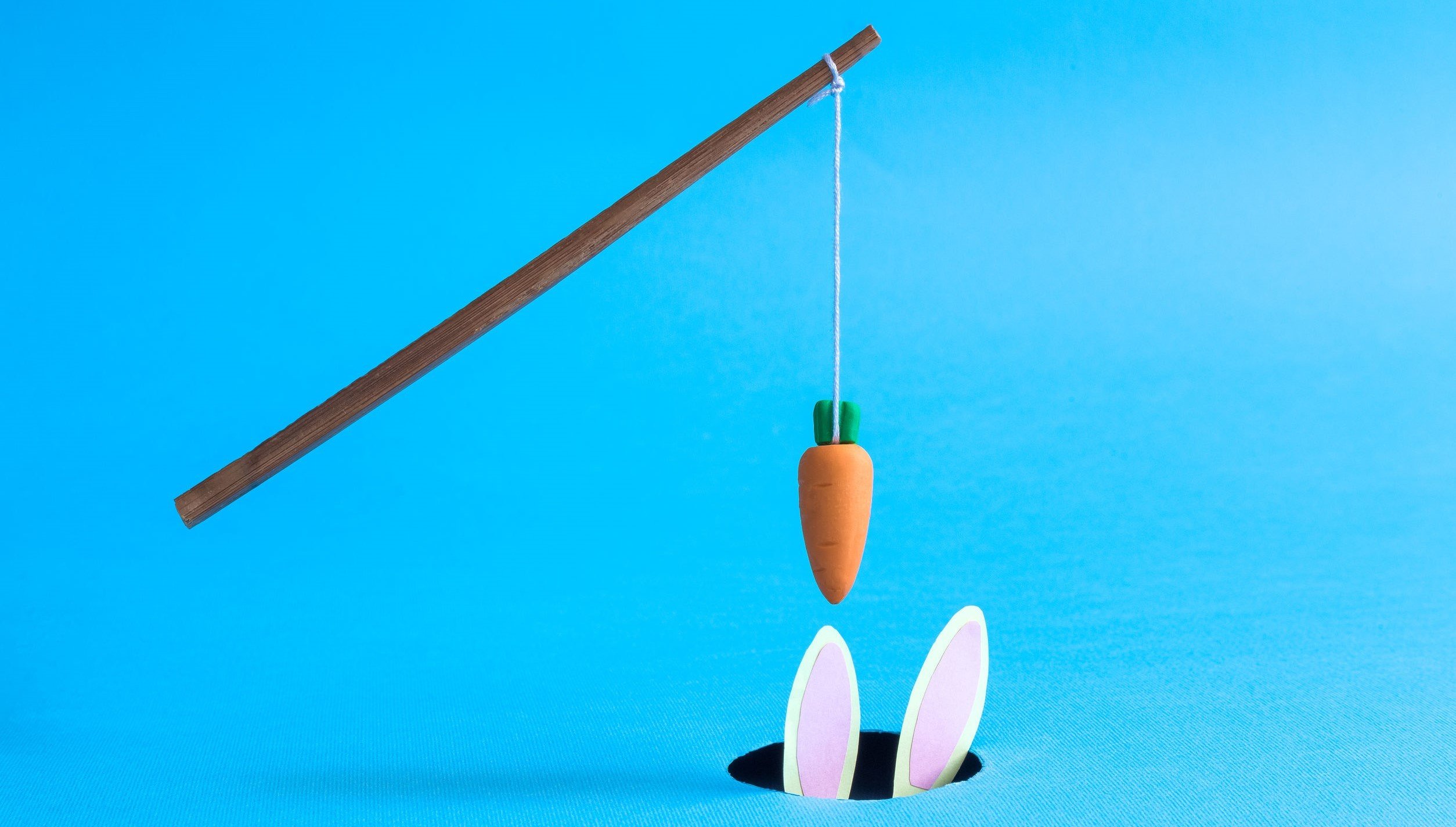 Orange carrot hanging on stick above black hole with rabbit in it abstract isolated on blue