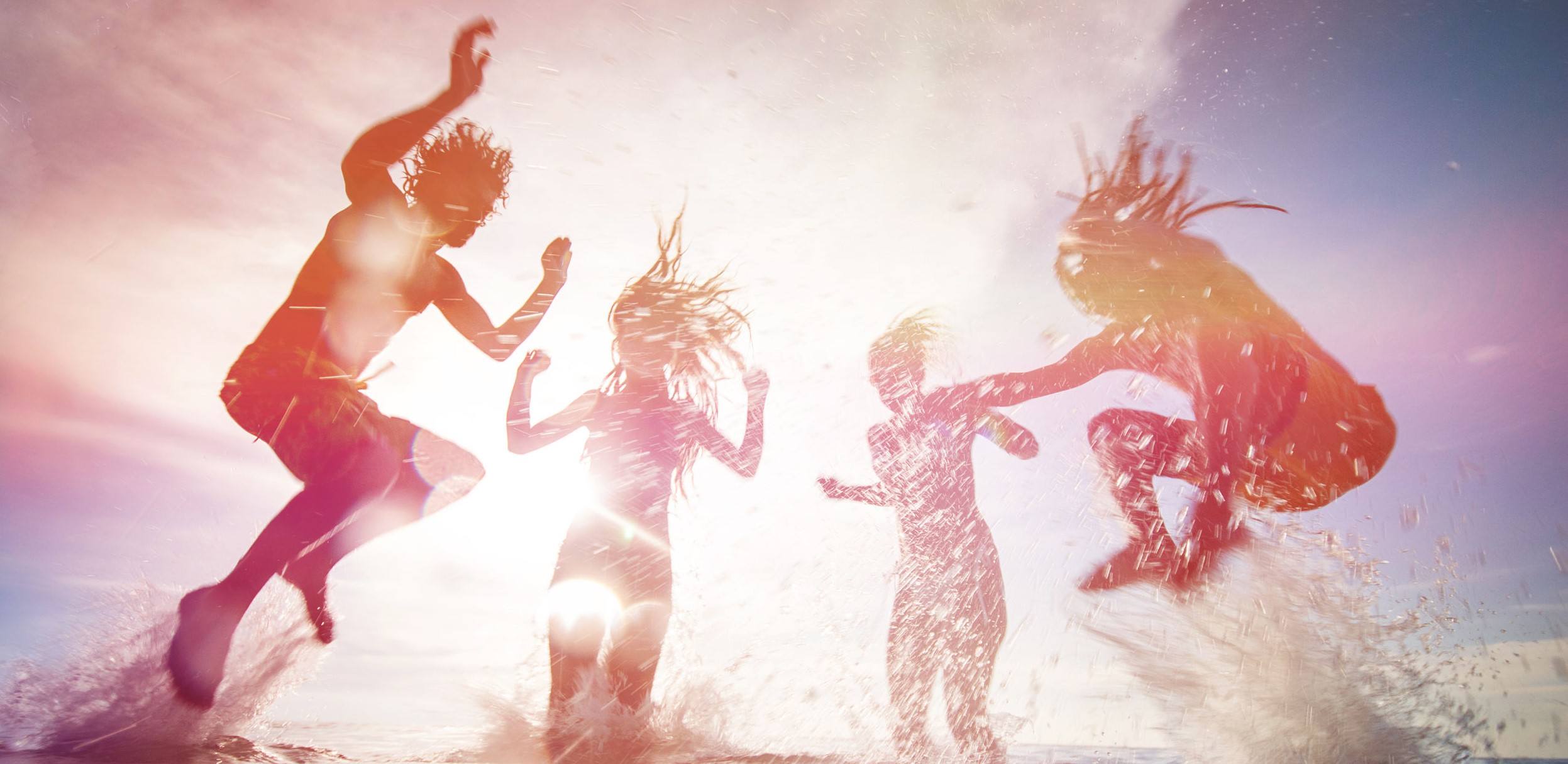 Silhouettes of happy young people jumping in sea
