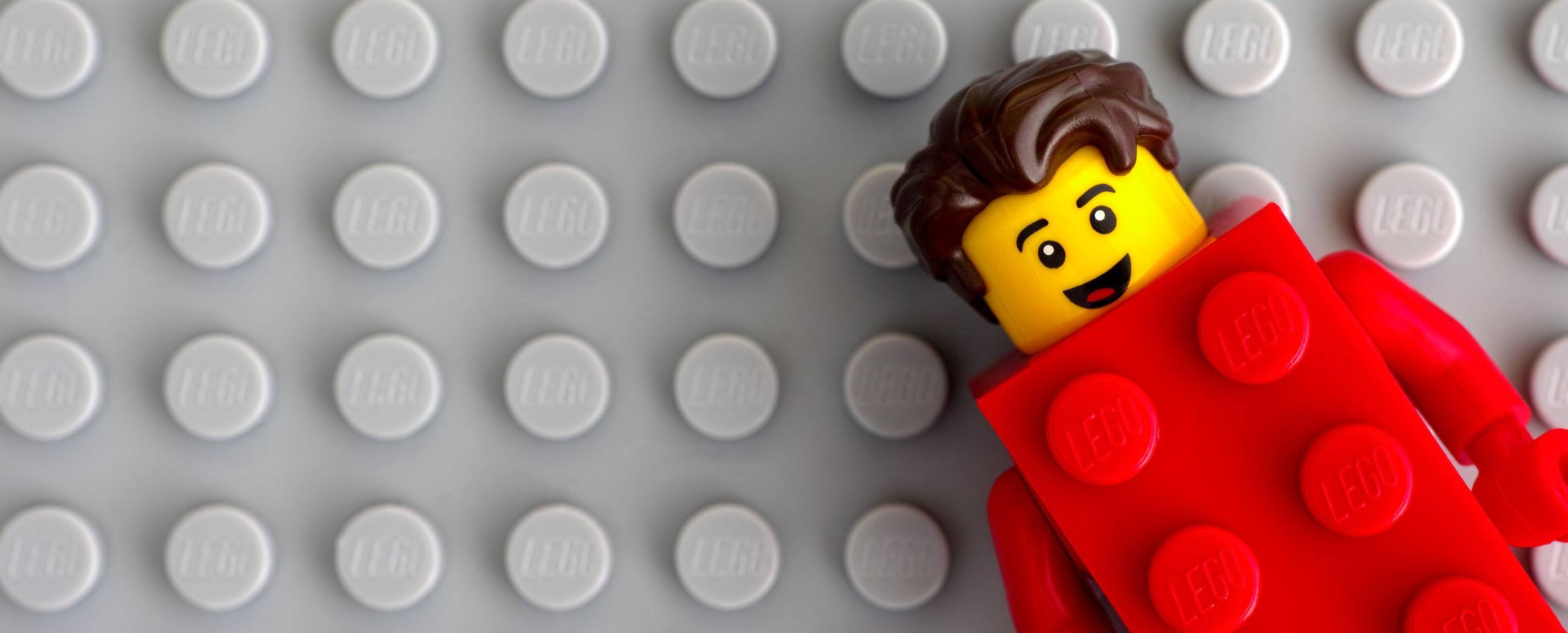 Lego Red Suit Brick Guy minifigure on gray baseplate background.