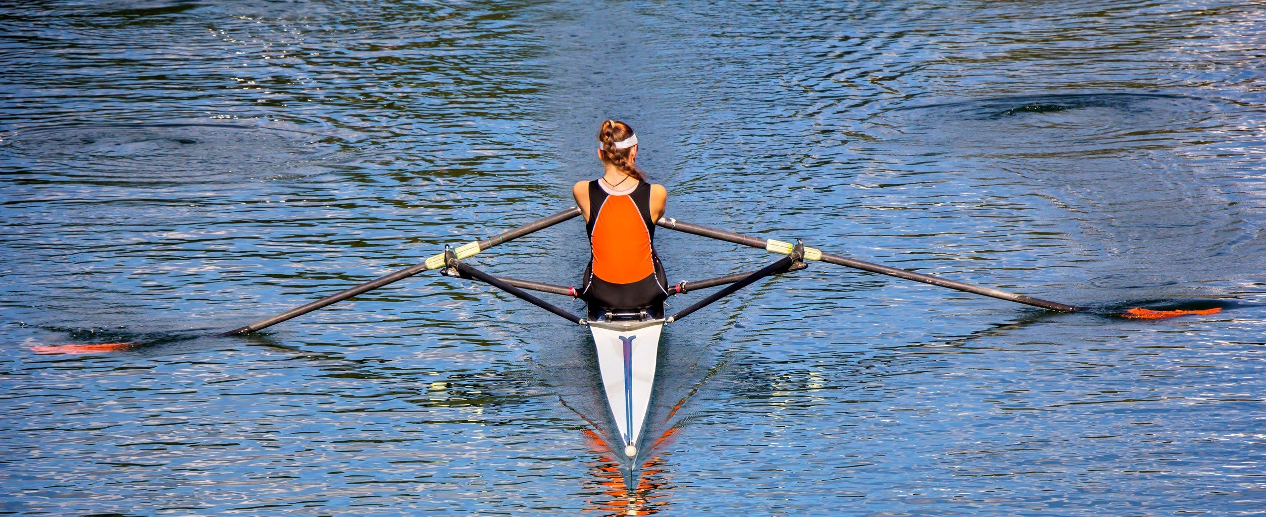 The woman rower in a boat, rowing on the tranquil lake