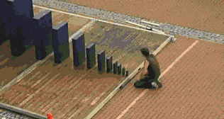 A man using one domino to knock over a bigger and bigger domino.